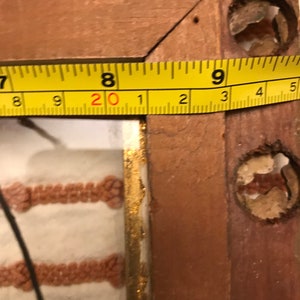 K&ouml;nnte beinhalten: Nahaufnahme eines Holzbildrahmens mit einem gelben Ma&szlig;band, das darum gewickelt ist. Das Band zeigt "20 1 2 3 4 5".