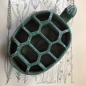 May include: A green ceramic turtle-shaped trinket dish with a honeycomb design. The dish has a small handle on the back.