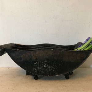 May include: A black metal planter with a curved shape and two handles. The planter is on wheels and has a distressed finish. It is filled with purple hyacinths.