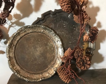 May include: Two silver serving trays with ornate edges. The smaller tray is on top of the larger tray. Both trays have a worn, aged look.