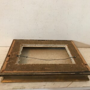 May include: A wooden picture frame with a gold-colored finish. The frame has a simple design with a flat surface and a slightly raised edge. The frame is in good condition, with some minor signs of wear.