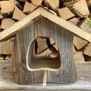 May include: A rustic wooden bird feeder with a peaked roof and a large opening for birds to access the food. The feeder is made of weathered wood and has a natural, rustic look.