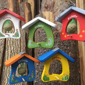 Könnte beinhalten: Fünf bunte Vogelhäuschen aus Holz. Jedes Häuschen ist in einer anderen Farbe bemalt: rot, weiß, grün, blau und gelb. Die Futterhäuschen haben eine hausähnliche Form mit einer kleinen Sitzstange und sind mit gemalten Blumen und dem Wort "Einkehr" verziert.