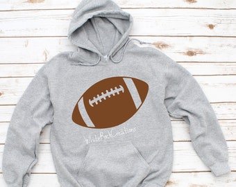 Peut inclure: Un sweat à capuche gris avec un motif de ballon de football marron et le texte "White Rock Creations" en blanc.