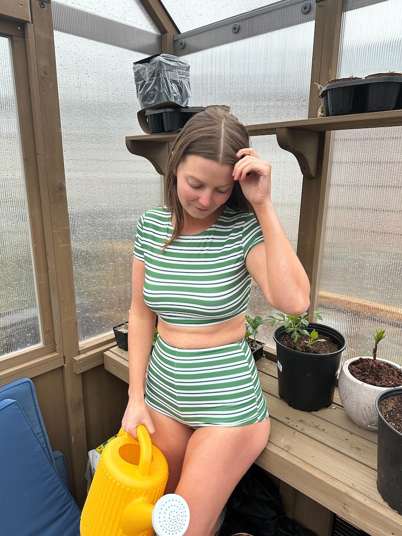 May include: A two-piece set consisting of a short-sleeved crop top and high-waisted shorts, both featuring a horizontal striped pattern in forest green and white. The set is made of a smooth, fitted fabric that sits against the body.