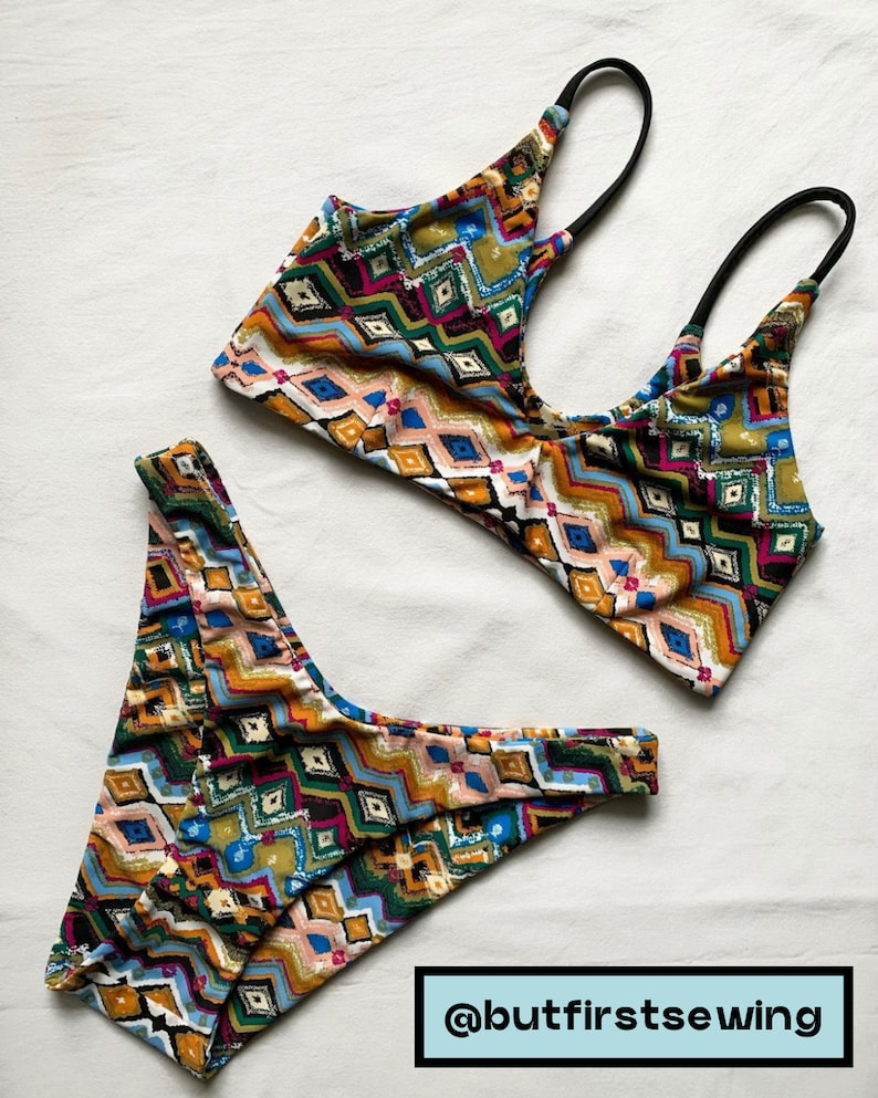May include: A two-piece swimsuit set with a colorful geometric pattern. The top has black straps and a scoop neck. The bottoms are a matching bikini cut. The fabric features a mix of blue, pink, yellow, and green diamond shapes.