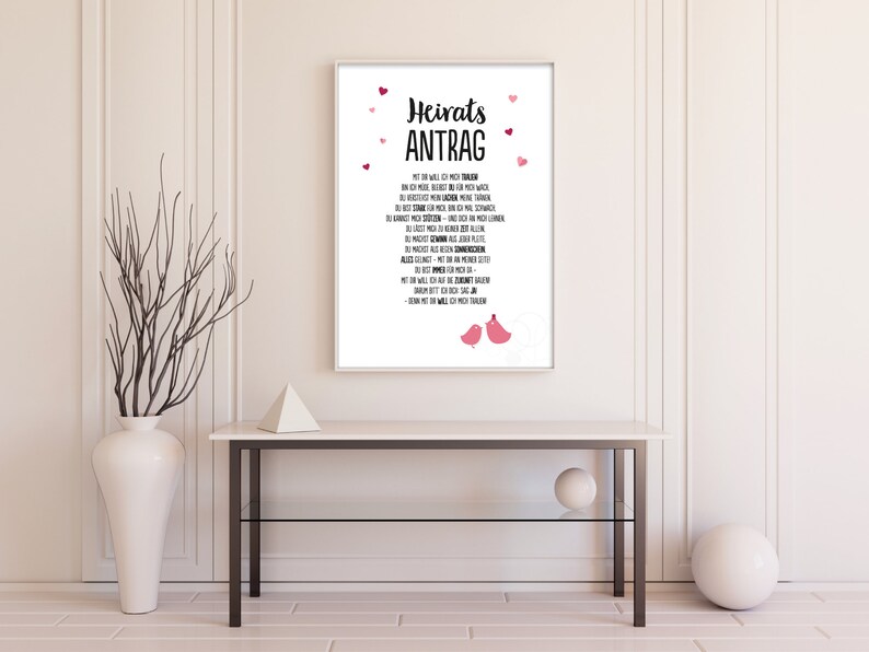 May include: A white framed print with a black and pink design. The print says "Heiratsantrag" and has a poem in German. The print is decorated with pink hearts and two pink birds.