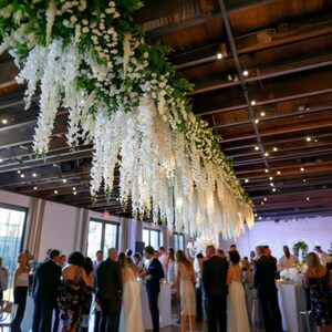 White wisteria artificial garland hanging from ceiling with soft, romantic lighting.