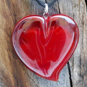 Op de afbeelding: Een rode glazen hart hanger met een zilveren beugel. Het hart is glad en glanzend, met een lichte bocht naar beneden.