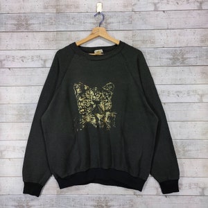 Op de afbeelding: Een zwart sweatshirt met een gouden luipaardprint op de voorkant. Het sweatshirt heeft een ronde hals en lange mouwen.