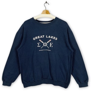 May include: A navy blue sweatshirt with a white graphic of the text "Great Lakes" and the letters "ΣΦΕ" with crossed oars underneath. The text "University of Minnesota" is below the oars.