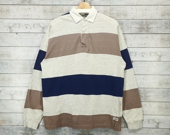 May include: A long-sleeved striped rugby shirt with brown, white, and blue horizontal stripes. The shirt has a button-up collar and a single button placket.
