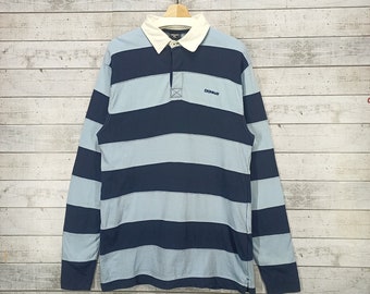 May include: A long-sleeved striped rugby shirt with a white collar and a navy blue and light blue striped pattern. The shirt has a button placket and a small logo that says "DONNER" on the chest.
