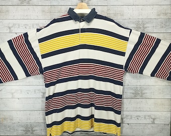 May include: A long-sleeved striped rugby shirt with a white, navy blue, red, and yellow color scheme. The shirt has a button-up collar and a small logo on the chest.