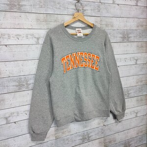 May include: Gray sweatshirt with a large orange "Tennessee" graphic on the front. The sweatshirt has a crew neck and long sleeves.