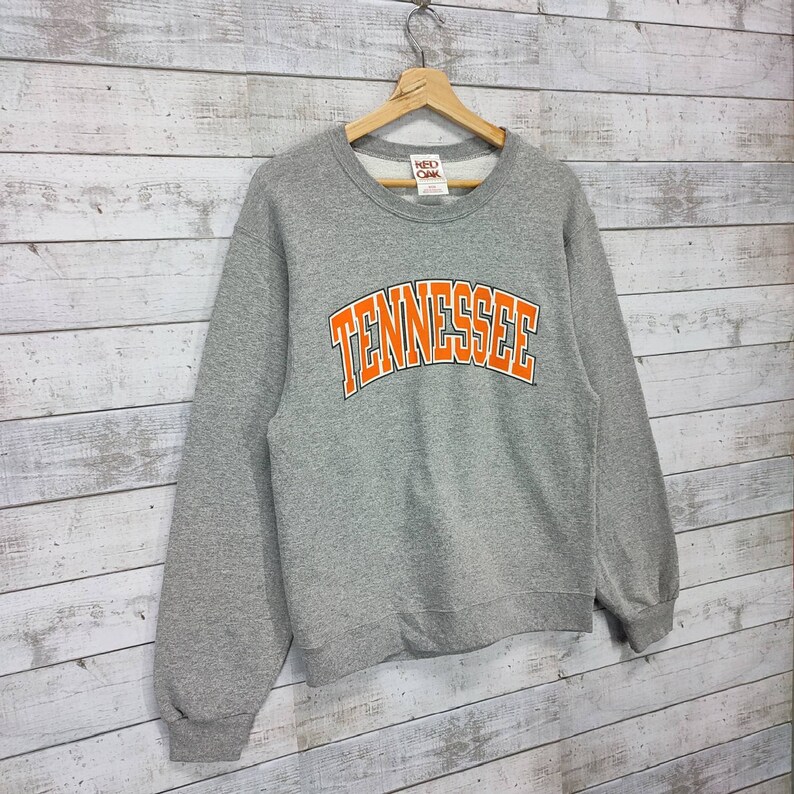 May include: Gray sweatshirt with a large orange "Tennessee" graphic on the front. The sweatshirt has a crew neck and long sleeves.