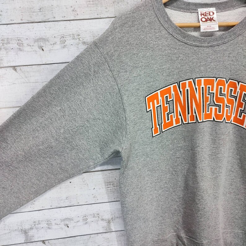 May include: Gray sweatshirt with a large orange "Tennessee" graphic on the front. The sweatshirt has a crew neck and long sleeves. The tag on the sweatshirt says "Red Oak".