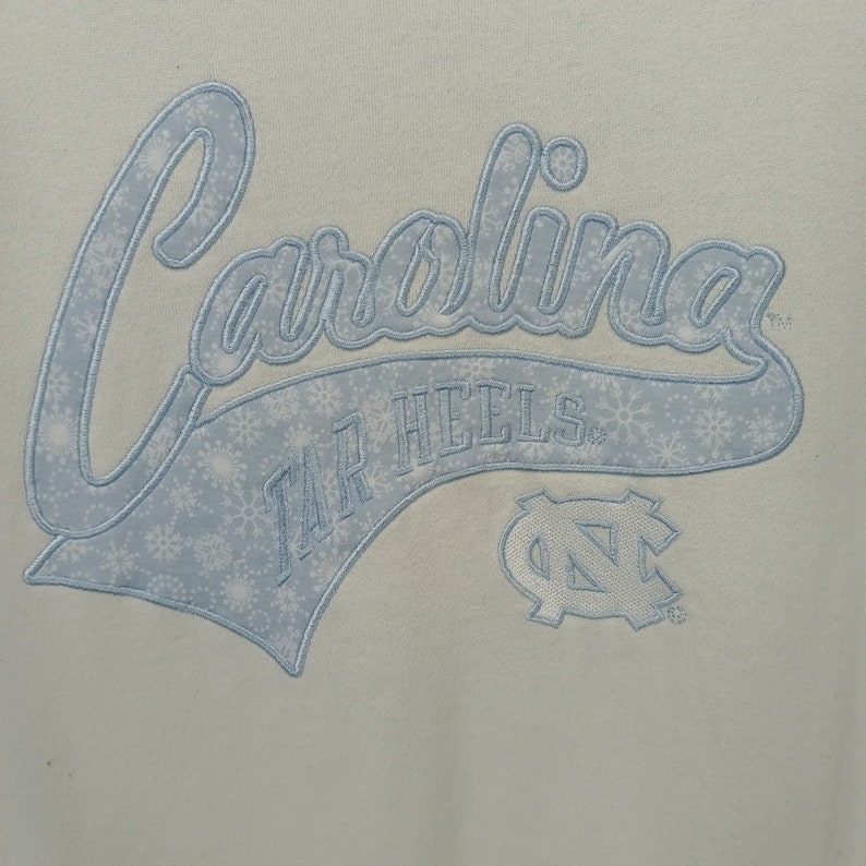 May include: White sweatshirt with a blue embroidered design that says "Carolina Tar Heels" with a blue and white UNC logo.