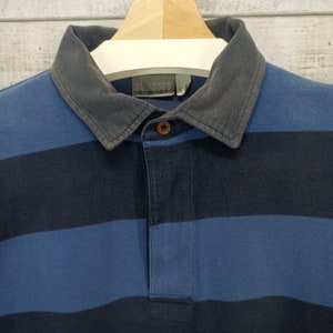 May include: Blue and black striped long-sleeve rugby shirt with a corduroy collar. The shirt has a button closure and a small label that reads "3L ISSES".
