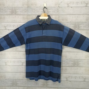 May include: A long-sleeved striped polo shirt with blue and black stripes. The shirt has a button-down collar and a single button placket.