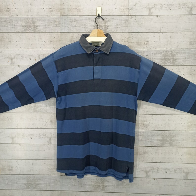 May include: A long-sleeved striped polo shirt with blue and black stripes. The shirt has a button-down collar and a single button placket.