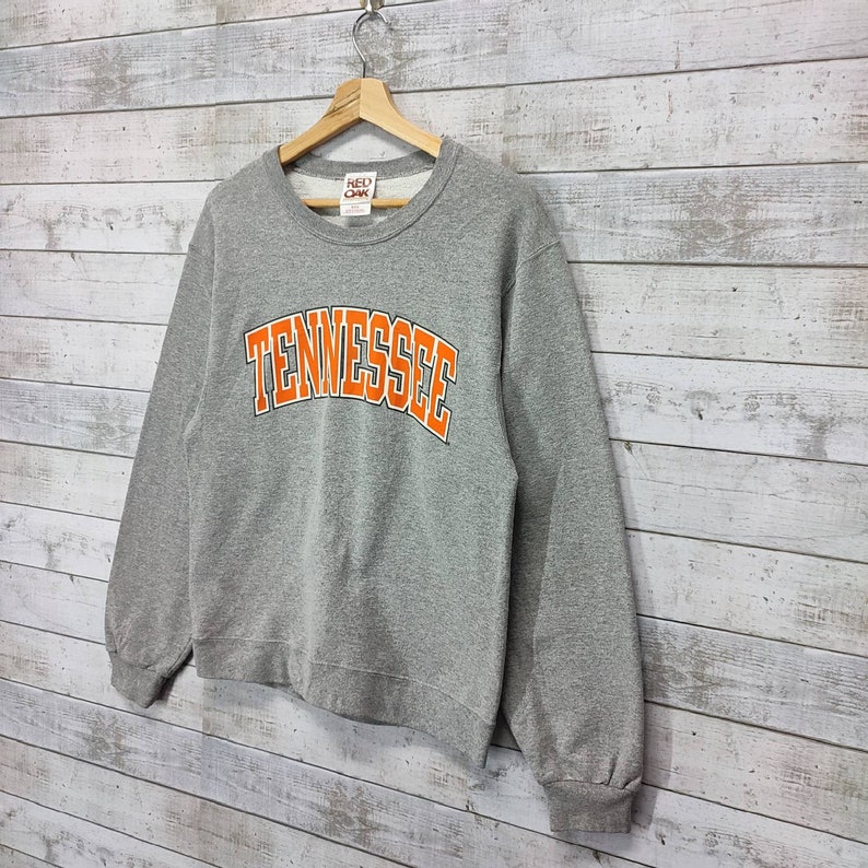 May include: Gray sweatshirt with a large orange "TENNESSEE" graphic on the front. The sweatshirt has a crew neck and long sleeves. The brand label "RED OAK" is visible on the front.