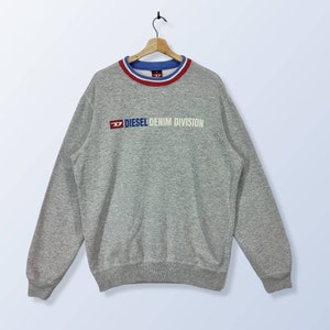 Könnte beinhalten: Grauer Pullover mit einem rot-weiß-blauen gestreiften Kragen und dem Schriftzug "DIESEL DENIM DIVISION" in weißen Buchstaben.