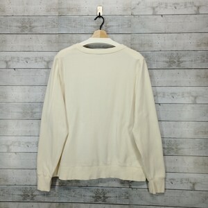 May include: A cream colored long-sleeved sweatshirt with a crew neck.