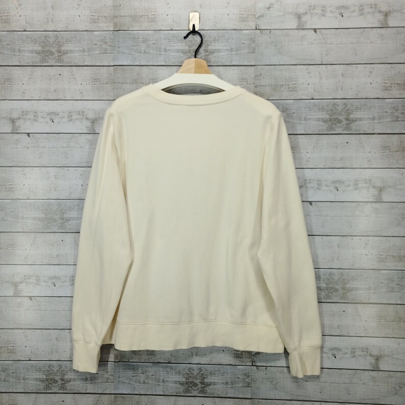 May include: A cream colored long-sleeved sweatshirt with a crew neck.
