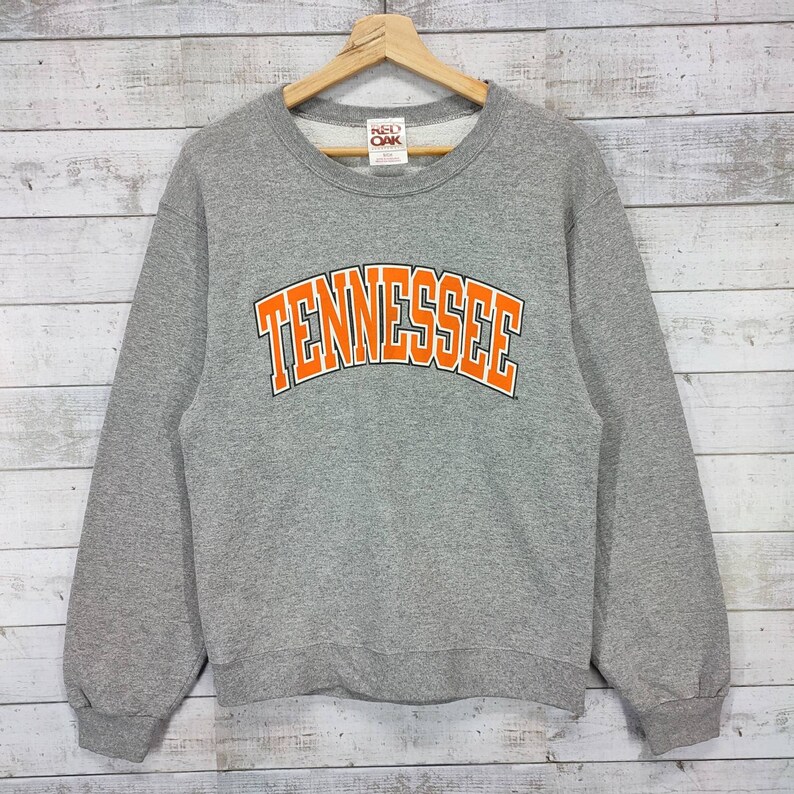 May include: Gray sweatshirt with an orange arch design that says "TENNESSEE" in a bold font. The sweatshirt has a Red Oak brand tag.