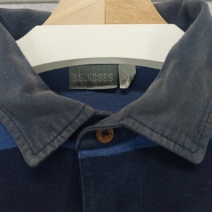 May include: A blue and black striped polo shirt with a dark blue collar and a label that reads "Swisses Le Chocolatier" and "87".