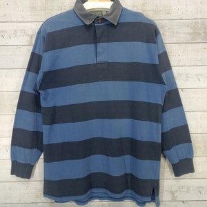 May include: A long-sleeved striped rugby shirt with a blue and black color scheme. The shirt has a button-up collar and a button placket.