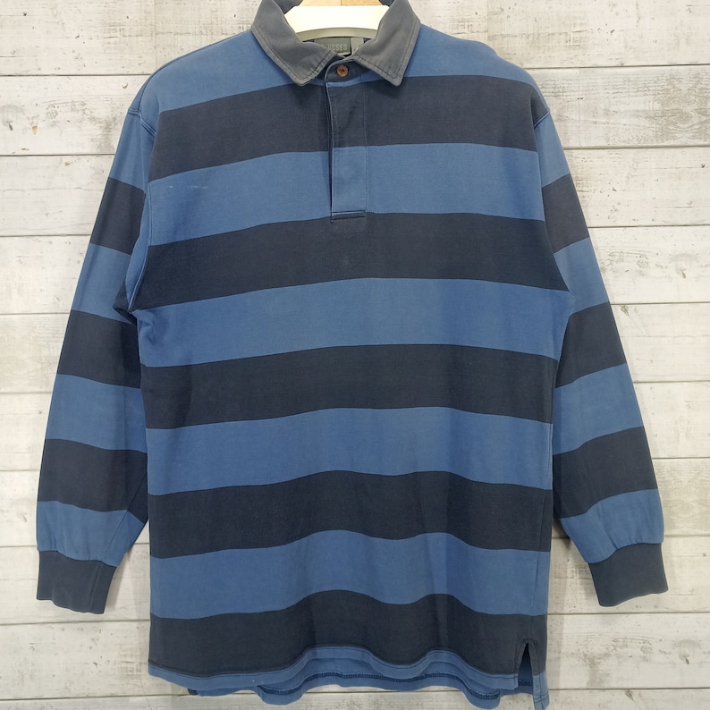 May include: A long-sleeved striped rugby shirt with a blue and black color scheme. The shirt has a button-up collar and a button placket.