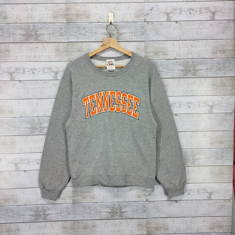 May include: Gray sweatshirt with a large orange "TENNESSEE" graphic on the front. The sweatshirt has a crew neck and long sleeves.