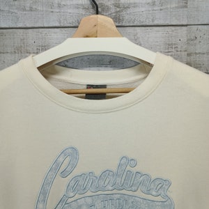 May include: A cream colored sweatshirt with a blue embroidered logo that says "Carolina" with snowflakes around the text.