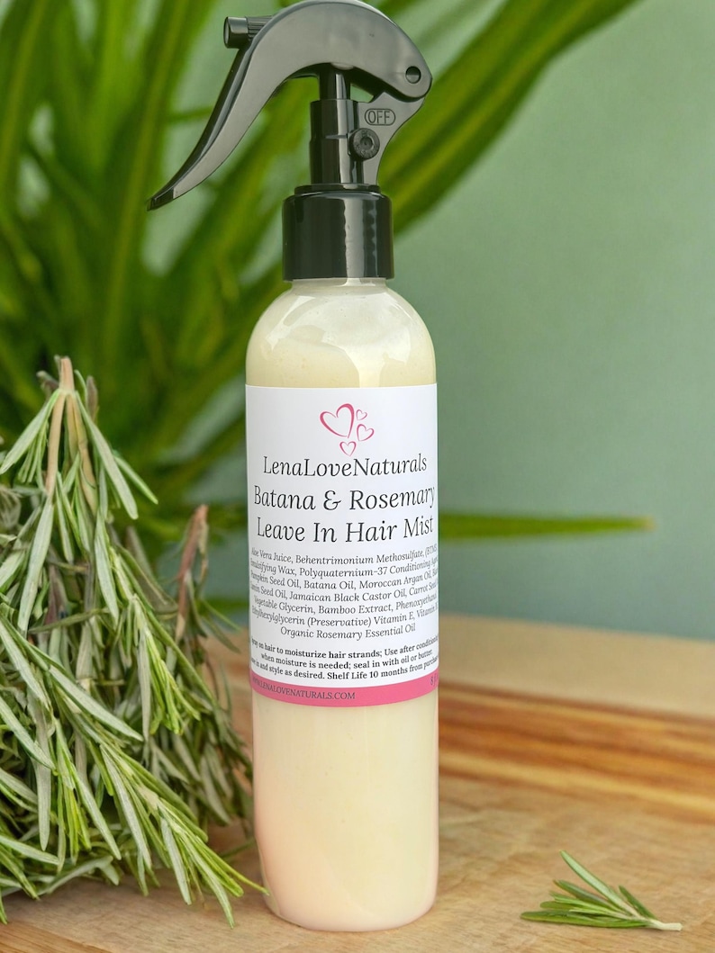May include: A clear spray bottle with a black nozzle labeled "OFF" contains a light yellow liquid. The label reads "LenaLoveNaturals Batana & Rosemary Leave In Hair Mist." Rosemary sprigs are in the foreground.
