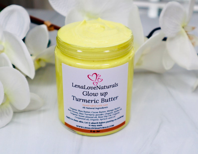May include: A yellow jar of turmeric butter labeled "LenaLoveNaturals Glow up Turmeric Butter" with the tagline "Handmade with Love". The jar is sitting on a white surface with white flowers in the background.