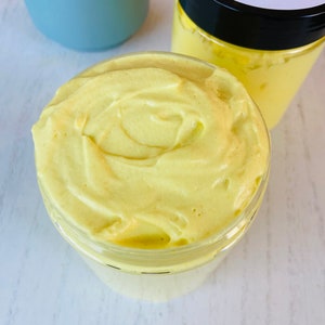 May include: A yellow turmeric butter in a clear glass jar with a black lid. The jar is filled with a thick, creamy butter. The label on the jar lists the ingredients: Organic Shea, Cocoa & Mango Butter, Raw Honey, Organic Jojoba oil, Organic Sweet almond oil, Rose Hip Oil, Organic Grapeseed oil, Organic Apricot seed oil. 8 oz Jar.