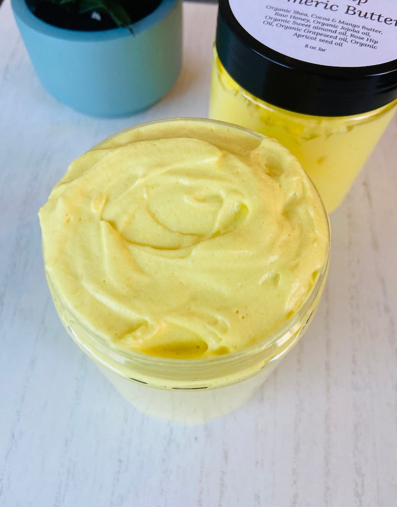 May include: A yellow turmeric butter in a clear glass jar with a black lid. The jar is filled with a thick, creamy butter. The label on the jar lists the ingredients: Organic Shea, Cocoa & Mango Butter, Raw Honey, Organic Jojoba oil, Organic Sweet almond oil, Rose Hip Oil, Organic Grapeseed oil, Organic Apricot seed oil. 8 oz Jar.