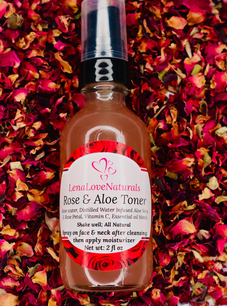 May include: A clear glass bottle with a black pump top filled with a rose-colored liquid. The bottle has a white label with the text "Lena Love Naturals Rose & Aloe Toner" and a list of ingredients. The bottle is sitting on a bed of red and pink rose petals.