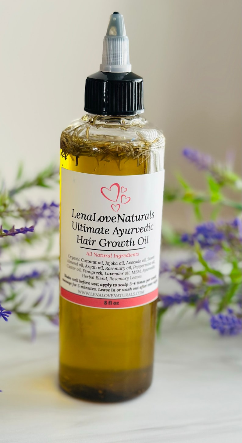 May include: A clear glass bottle with a black cap and a pink label that reads "Lena Love Naturals Ultimate Ayurvedic Hair Growth Oil". The label lists all natural ingredients and instructions for use. The bottle is sitting on a white surface with purple flowers in the background.
