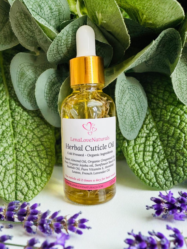 May include: A clear glass bottle of Lena Love Naturals Herbal Cuticle Oil with a gold cap and white dropper. The label lists ingredients like Sweet Almond Oil and French Lavender Oil. The bottle is surrounded by green leaves and purple flowers.