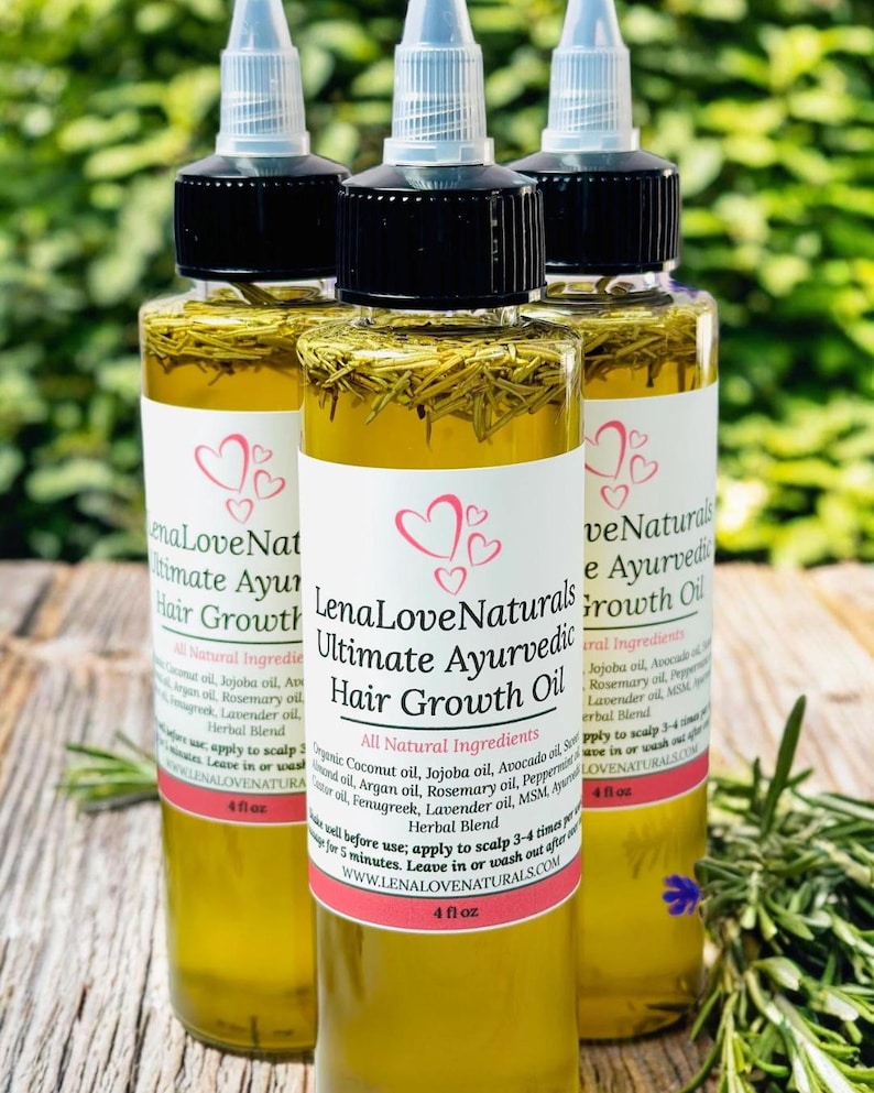 May include: Three amber glass bottles with black caps and white labels. The labels have a pink heart design and the text "LenaLoveNaturals Ultimate Ayurvedic Hair Growth Oil". The bottles are sitting on a wooden surface with green foliage in the background. All Natural Ingredients.