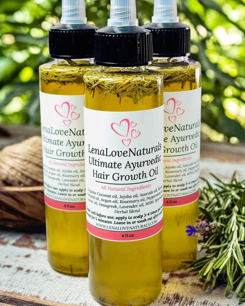 May include: Three 4-ounce bottles of Lena Love Naturals Ultimate Ayurvedic Hair Growth Oil. The bottles are clear glass and contain a yellow liquid. The labels are white with pink hearts and black text. The bottles are sitting on a wooden surface with green foliage in the background.