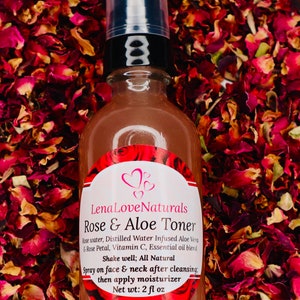 May include: A brown glass bottle with a black pump top and a white label that reads "Lena Love Naturals Rose & Aloe Toner". The bottle is surrounded by rose petals.