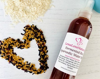 Może przedstawiać: Brązowa szklana butelka z białą etykietą, na której widnieje napis "LenaLoveNaturals Fermented Rice Ayurvedic Water Spray" i lista składników, w tym MSM, biotyna, kolendra, aloes, witamina B5, liście hibiskusa, korzeń prawoślazu, brahmi, korzeń łopianu i sorbat. Butelka stoi na białym tle z sercem ułożonym z suszonych ziół.