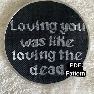 Könnte beinhalten: Schwarzer Stickrahmen mit weißem Text, der "Loving you was like loving the dead." lautet.  PDF Pattern steht in der unteren rechten Ecke.