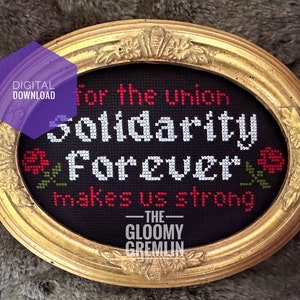 Könnte beinhalten: Eine gerahmte Kreuzstich-Stickerei mit schwarzem Stoff und weißen und roten Buchstaben, die "For the union Solidarity Forever makes us strong - THE GLOOMY GREMLIN" lautet.