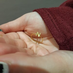 May include: A gold ring with the letter "N" on it. The ring is on a person's hand.