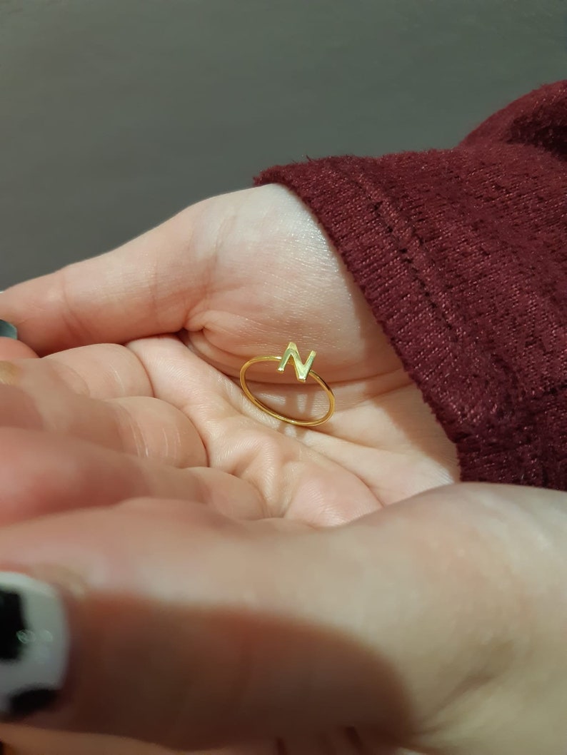 May include: A gold ring with the letter "N" on it. The ring is on a person's hand.